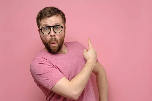 Man in glasses points with index finger to a copy of the space and looks at the camera with an surprised expression on face.