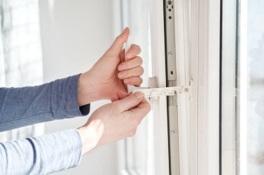 Female hands fix with a special device an open for ventilation, modern PVC window, in natural light.