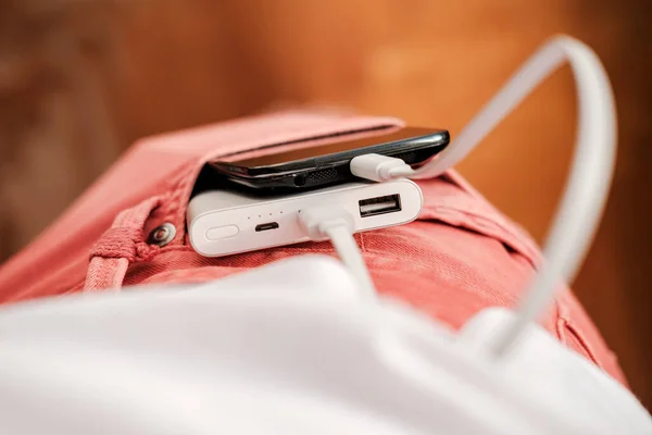 Banco de energía y un teléfono móvil que se está cargando se encuentra en el bolsillo delantero de los pantalones vaqueros de color coral. Vista superior . —  Fotos de Stock
