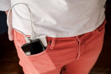 Enerji bankası ve şarj olan bir cep telefonu mercan renkli kotun ön cebinde yatıyor..