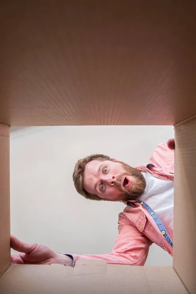 Contented, joyful bearded man unpacks a delivered box with a parcel or a gift. Unboxing inside view. Copy space.