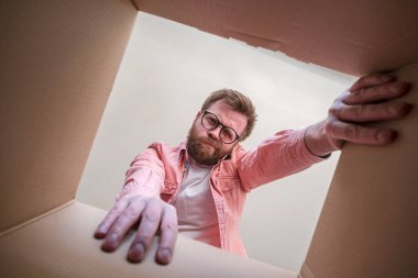 Gözlüklü bir adam, içinde hoşnutsuzluk ve hayal kırıklığıyla dolu bir paket olan paketsiz teslim edilmiş bir kutuya bakar. İçerideki kutucuğu aç.