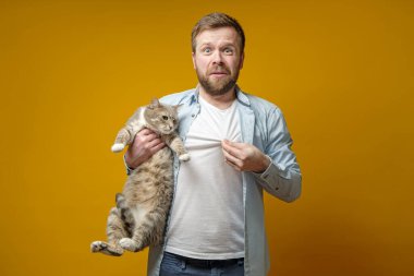 Üzgün adam bir kedi tutar ve üzerinde tüylü bir hayvanın kürkü olan tişörtünü gösterir..