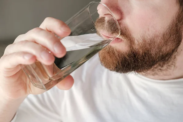 Primer plano de un hombre barbudo bebiendo agua fresca y limpia de un vaso. Concepto de salud . —  Fotos de Stock