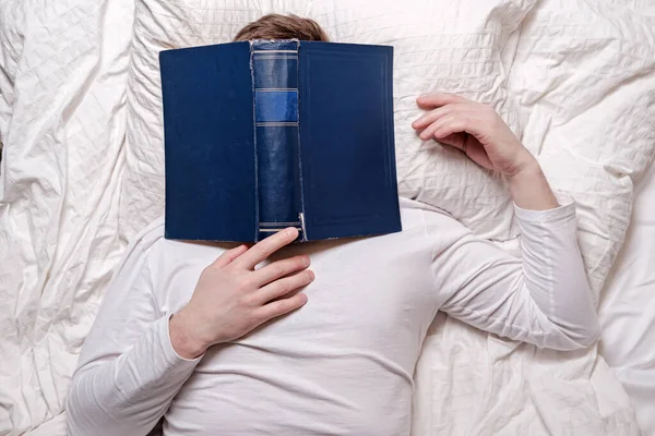 El hombre en pijama se durmió leyendo y el libro se cubrió la cara. Concepto educativo. Vista superior . — Foto de Stock