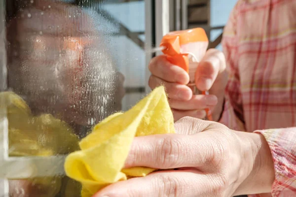 Die weibliche Hand wäscht an einem sonnigen Tag Fensterscheiben mit einem Spray mit Reinigungsmitteln und Lumpen von Staub und Schmutz. Konzept der Sauberkeit. — Stockfoto