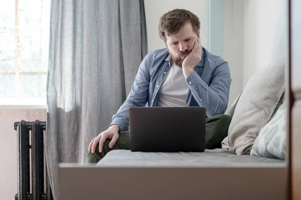 Mannen med en bärbar dator är uttråkad när han sitter hemma. Han är ledsen för att han tvingas stanna hemma under en virus- och pandemisk epidemi.. — Stockfoto