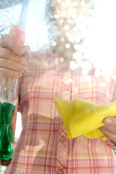 Vrouw wast op een zonnige lentedag een vensterglas van stof en vuil, met behulp van een spray met wasmiddelen en vodden. Concept van reinheid. — Stockfoto