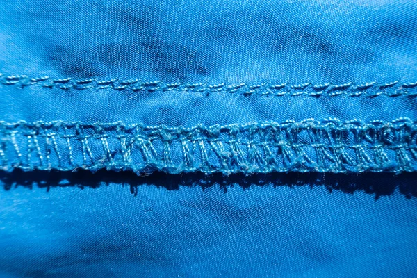 Cucitura overlock su tessuto sintetico blu. Macro. Vista dall'alto . — Foto Stock