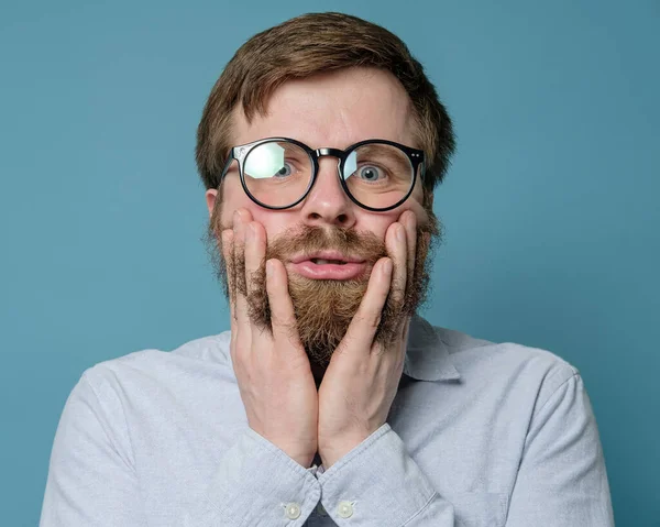 Un hombre gracioso con gafas puso los dedos en su barba peluda. Está molesto porque no puede visitar la barbería debido a la cuarentena. . — Foto de Stock