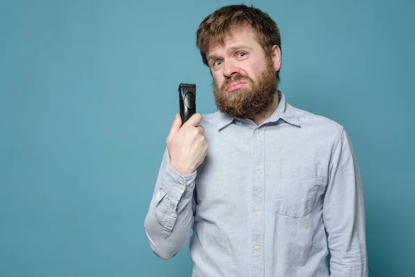 Divertente uomo shaggy con un trimmer non è stato nel barbiere per molto tempo e dovrà tagliarsi. Concetto di quarantena . — Foto Stock