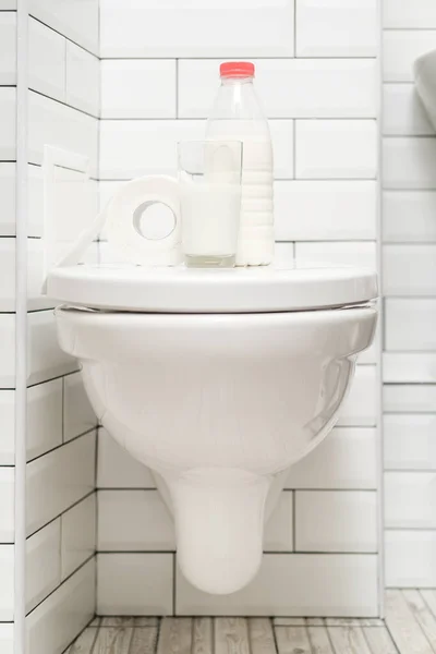 Nietolerancja laktozy. Szklanka mleka, butelka nabiału i rolka papieru toaletowego są na muszli klozetowej. Zdjęcie pionowe. — Zdjęcie stockowe