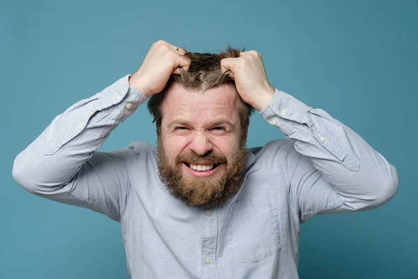 El hombre está enojado y experimentando estrés, se arranca furiosamente el pelo y sonríe. Concepto de salud mental . — Foto de Stock