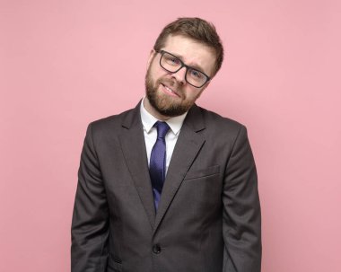 Gözlüklü ve takım elbiseli yorgun beyaz adam alaycı bir şekilde gülümsüyor ve kayıtsızca kameraya bakıyor..