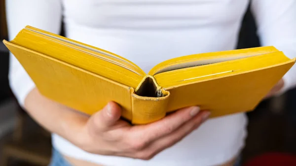 Öppen tjock, gammal gul bok hålls av kvinnliga händer, på en suddig bakgrund. — Stockfoto