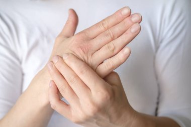 Kadın elinde ağrı hissediyor ve beyaz bir tişörte hassas bir noktaya masaj yapıyor..