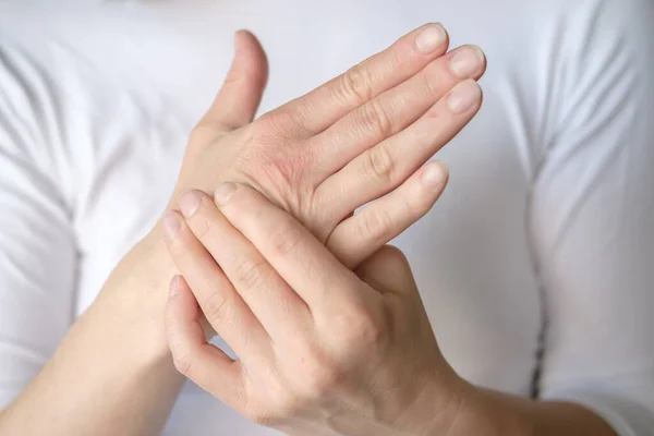 Frau spürt Schmerzen in der Hand und massiert wunde Stelle gegen weißes T-Shirt. — Stockfoto