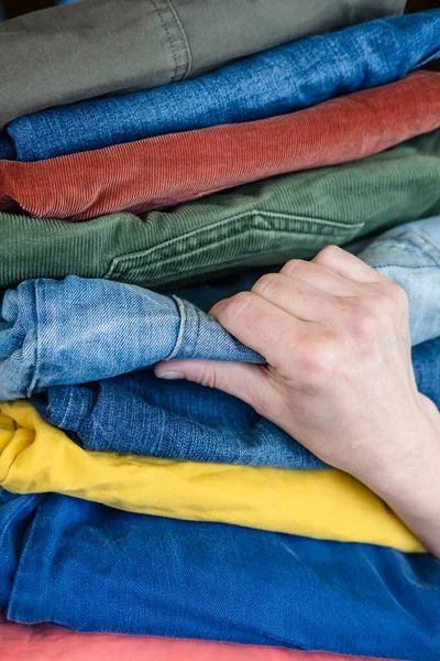 Female hand picks jeans from a stack of neatly folded trousers in bright colors. — Stock Photo, Image