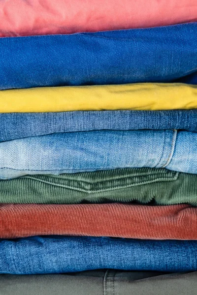 Pila de jeans y pantalones cuidadosamente doblados en colores brillantes. Fondo abstracto . — Foto de Stock