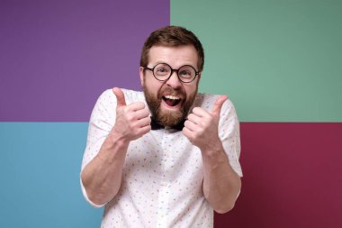 Weird, cheerful man in round glasses makes an approving gesture with hands, thumbs up with a funny grimace on face. clipart