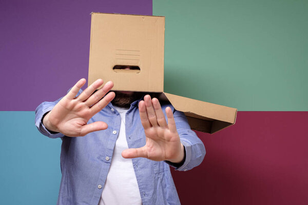 Weird, scared man with a box on his head makes a stop gesture. Concept of fear of society and shelter from problems.