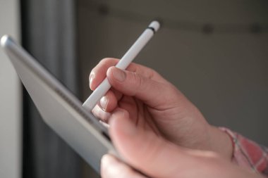 Kadın eli, dijital tablet üzerinde bulanık bir arkaplanda stilus kalemle yazar veya çizer..