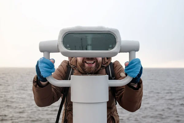 Gioioso, sorridente uomo guarda con interesse lo spettatore torre, in piedi sul lungomare, sullo sfondo del mare . — Foto Stock