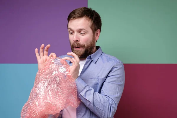 Young, funny man popping a bubble wrap as a therapy and calms down after experiencing stress. — Stock Photo, Image