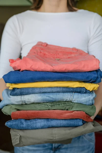 Kobieta trzyma schludnie złożone spodnie i dżinsy w jasnych kolorach, po praniu, w pralni. — Zdjęcie stockowe