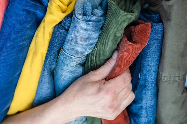 Vrouwelijke handenstokers rood fluwelen broek van een stapel keurig gevouwen jeans in felle kleuren. — Stockfoto