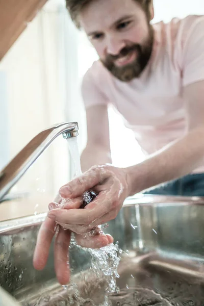 Hands under a stream of clean water, on a blurred background, a smiling man observing the rules of hygiene. Health concept.