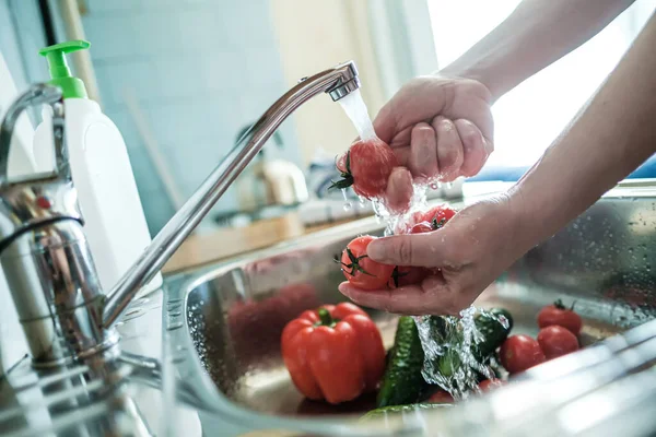 Female hands wash red tomatoes under a stream of water, against the background of vegetables in the sink. Cooking food. — Stock Photo, Image