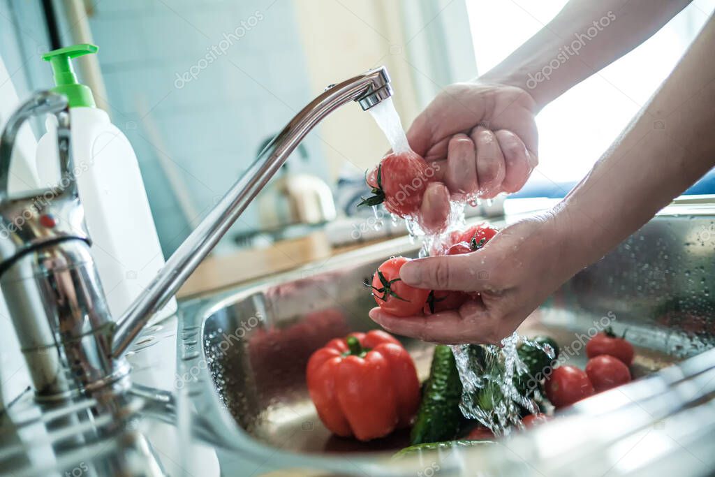 Female hands wash red tomatoes under a stream of water, against the background of vegetables in the sink. Cooking food.