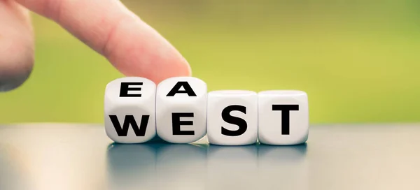 Mão vira um dado e muda a palavra "leste" para "oeste", ou vice — Fotografia de Stock