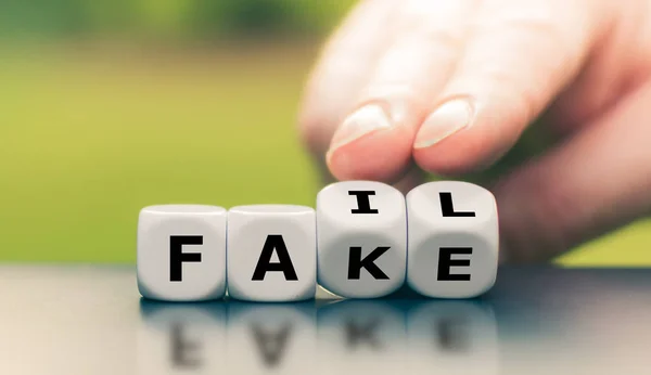 Hand turns a dice and changes the word "fake" to "fail". — 스톡 사진