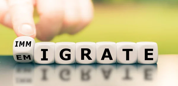Mão vira um dado e muda a palavra "imigração" para "emigrante — Fotografia de Stock