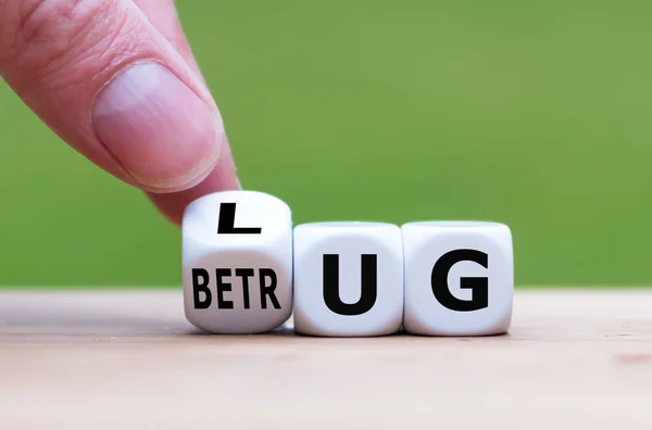 Hand turns a dice and changes the German word "LUG" ("lie" in En — 스톡 사진