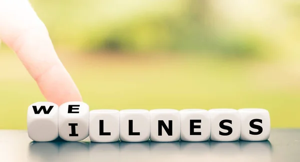 Hand turns dice and changes the word "illness" to "wellness". — 스톡 사진