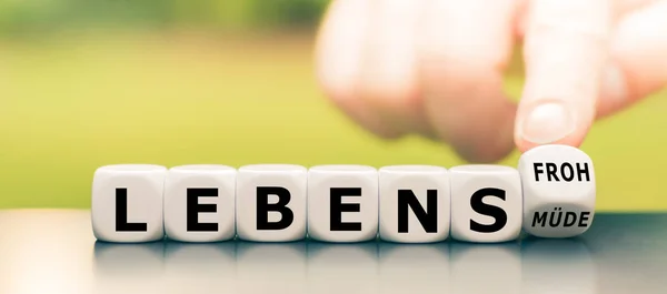 Hand turns a dice and changes the German word "lebensmuede" ("tired of life) to "lebensfroh" ("full of joy"). — Stock Photo, Image