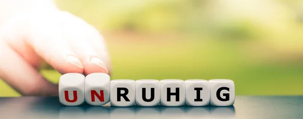 La mano gira los dados y cambia la palabra alemana "unruhig" ("espasmódico " — Foto de Stock