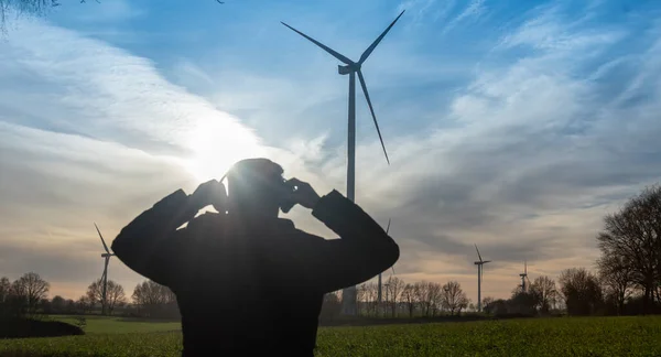 Engineer standing in front of a wind turbine during sunset.