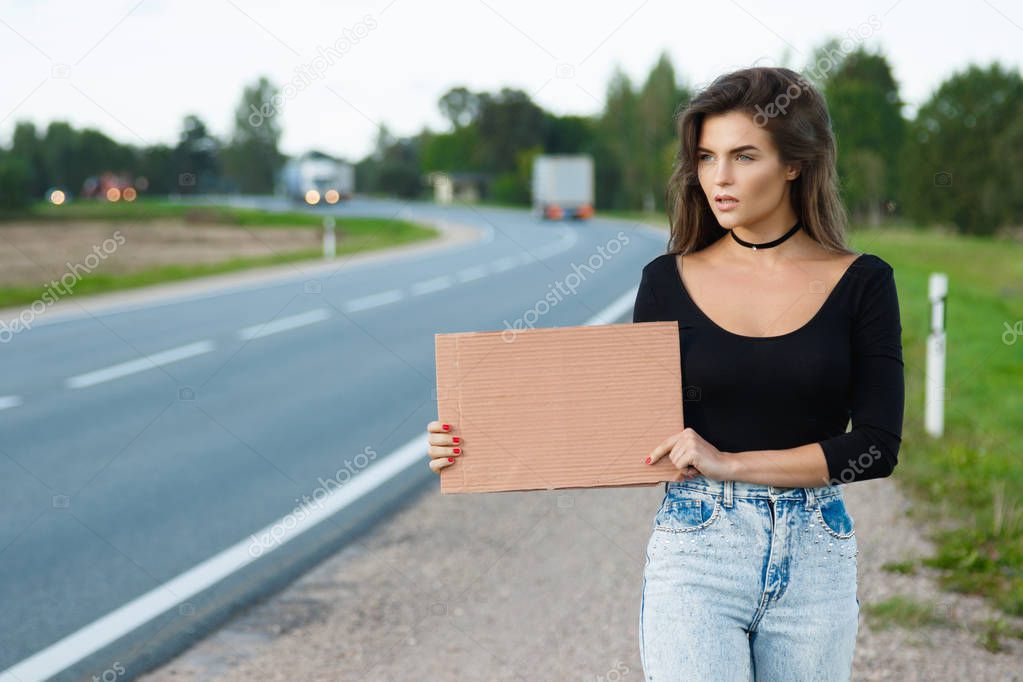 Young woman hitchhiker on road 