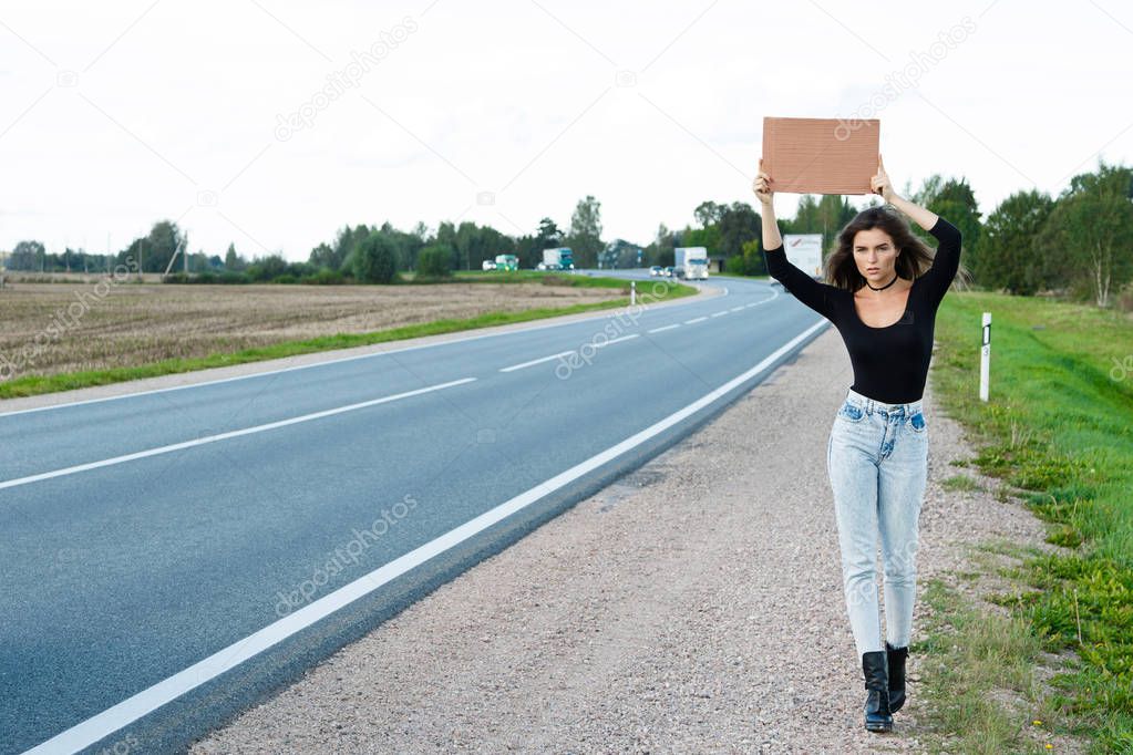 Young woman hitchhiker on road 
