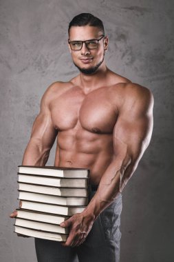 Bir yığın kitabı olan zeki ve kaslı bir adam. Vücut geliştirmede bilgi kavramı.