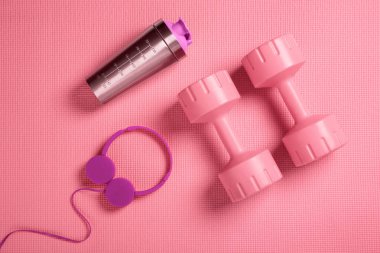 Fitness minderinde pembe dambıllar, kulaklıklar ve protein karıştırıcı.