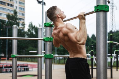 Genç ve kaslı adam yatay çubukta barfiks çekiyor.