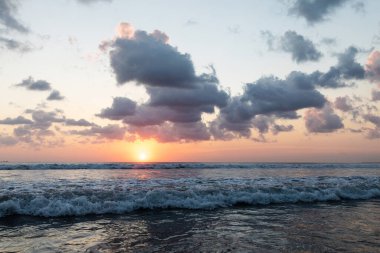 Sahilde güzel bir gün batımı. Bulutlu, dalgalı ve güneşli deniz manzarası.