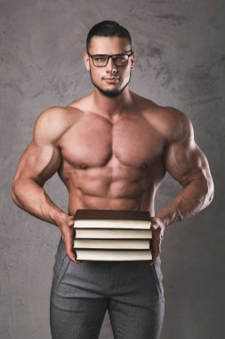 Bir yığın kitabı olan zeki ve kaslı bir adam. Vücut geliştirmede bilgi kavramı.