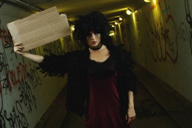 Karanlık tünelde elinde boş bir karton parçasıyla tuhaf ve tuhaf bir kadın.