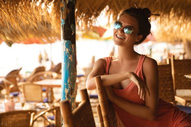 Sıcak yaz gününde plaj barında oturan güneş gözlüğü takan genç bir kadın.